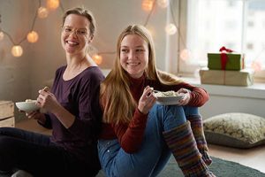 Äiti ja tytär istuvat olohuoneessa hymyillen.