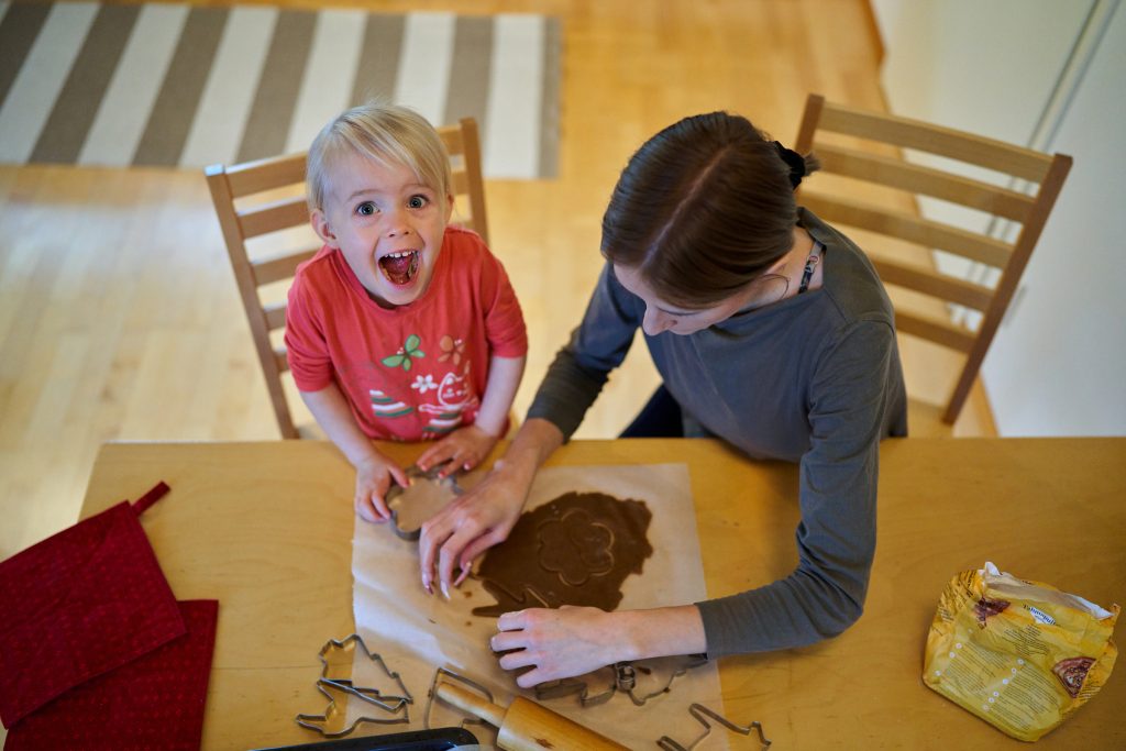 Lapsi ja äiti ovat leipomassa pipareita. Lapsi katsoo kameraan yllättyneellä ilmellä.