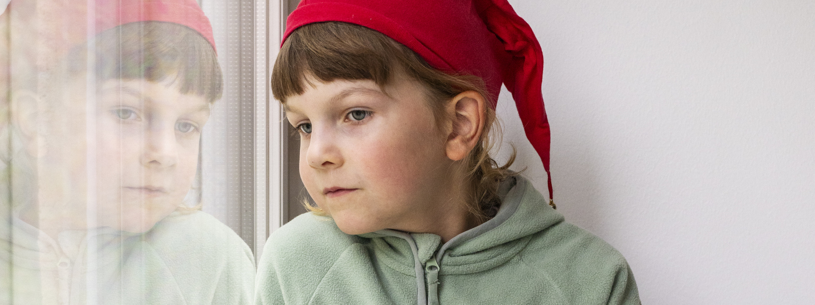 lapsi katsoo ulos ikkunasta tonttulakki päässä